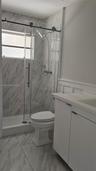 Walk-in shower with sliding glass door, stone-finish wall tile, white vanity with integrated sink, and wainscoting detail