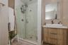Walk-in shower with stone-finish wall tile, pebble-style flooring, and frameless glass door