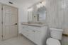 Double vanity featuring white cabinetry, stone-patterned countertop, arched mirrors, metallic hardware, and floor-to-ceiling cabinetry