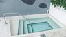 Inground plunge pool featuring white tile lining, multi-level stairs, stainless steel handrail, and stone tile surround