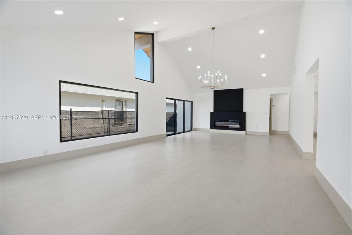Kitchen featuring shaker-style cabinetry, an expansive center island with stone-finish countertops, matte black appliances, modern multi-globe chandel