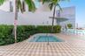 In-ground spa with a metal handrail, geometric patterned tile decking, mature palm trees, and manicured privacy hedging