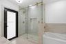 Walk-in shower with frameless glass enclosure, gold-toned hardware, stone-tile surround, and recessed wall niche, featuring a separate white soaking t