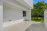 Modern exterior patio featuring large-format porcelain tile flooring, expansive floor-to-ceiling sliding glass panels, smooth white stucco finish, and