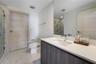 Modern vanity with a light-toned countertop, integrated basin, and dark wood-finish cabinetry, paired with large-format stone-finish floor tile, a ful