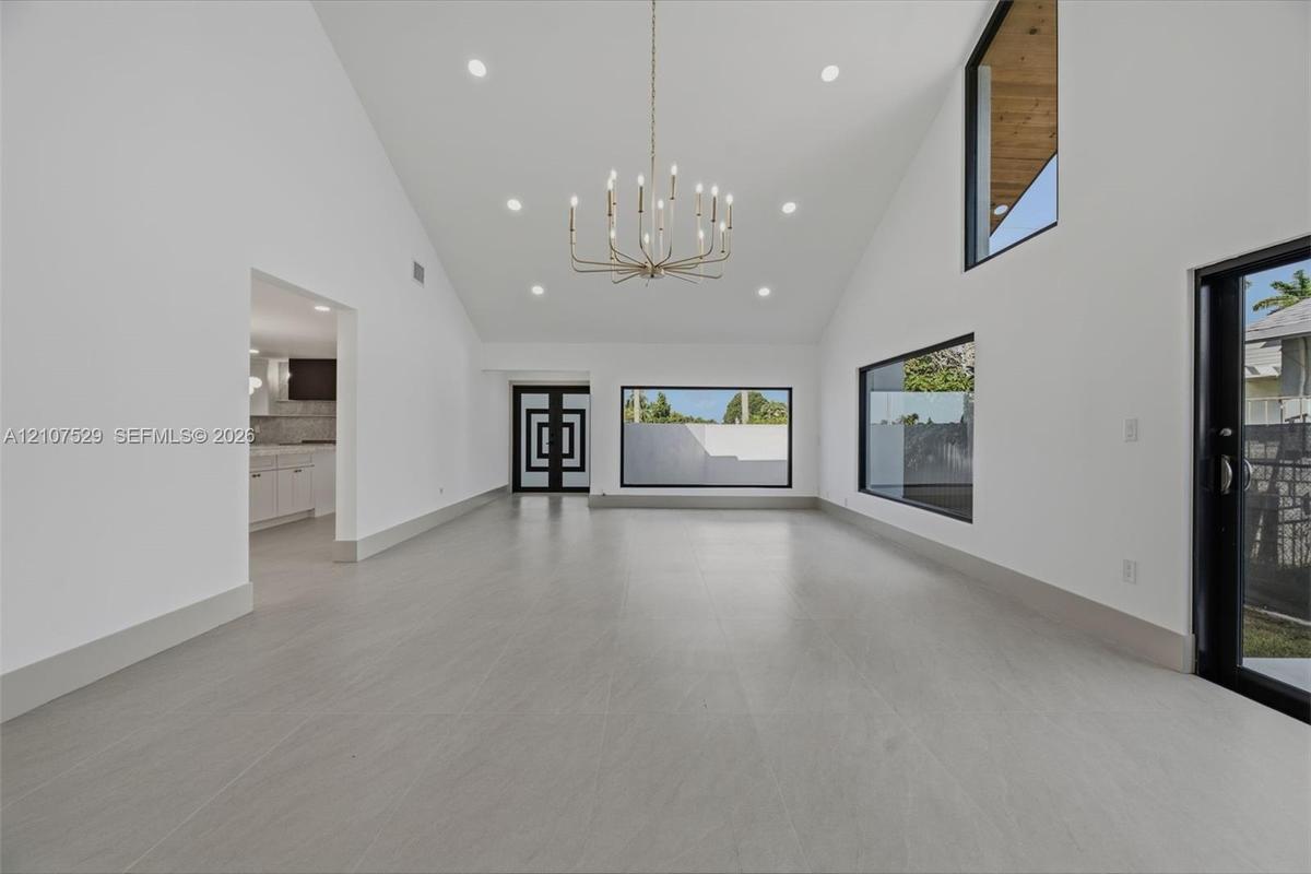 Neutral-toned interior featuring large-format flooring, recessed lighting, a multi-arm chandelier, and expansive sliding glass doors