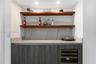 Custom wet bar featuring charcoal-toned cabinetry, a stone-patterned countertop and backsplash, dual wood-finish floating shelves, and a built-in wine