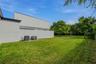 Modern exterior with a smooth white stucco finish, expansive manicured lawn, and a covered outdoor patio featuring wood-paneled ceiling detailing