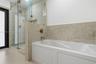 Dual-sink vanity with white cabinetry and stone-finish countertops, glass-enclosed shower with gold-tone hardware, pebble-stone shower flooring, and a
