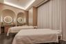Dual vanity area featuring stone-topped counters with integrated cabinetry, recessed arched wall niches, circular backlit mirrors, and recessed tray c