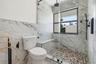 Dual-vanity cabinetry with stone-finish countertops, arched vanity mirrors, multi-bulb lighting, wall-mounted matte black faucet, and a freestanding s