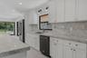 Kitchen featuring white shaker-style cabinetry, a large island with integrated microwave, stone-finish countertops and backsplash, black matte range w