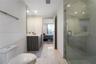 Bathroom featuring a dark wood-finish vanity, light-toned stone-style tile flooring, floor-to-ceiling vanity mirror, and a glass-enclosed shower with 