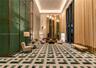 Grand lobby featuring double-height ceilings, intricate green geometric wall cladding, full-height window treatments, and patterned stone flooring