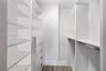 Walk-in closet featuring white built-in shelving, integrated dresser drawers with bar pulls, and a metal hanging rod over wood-finish flooring