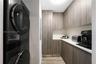 Utility room featuring stacked laundry appliances, wood-finish cabinetry, white solid-surface countertops, and wood-finish flooring