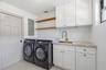 White shaker-style cabinetry with brass-tone hardware, stone-finish countertop, neutral large-format flooring, and drum-style ceiling fixture