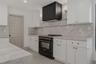 Kitchen featuring white shaker cabinetry, stone-finish countertops and backsplash, black range with matching vent hood, and natural wood floating shel