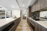 Modern kitchen featuring wood-finish cabinetry, white countertops, built-in stainless steel appliances, a mirrored backsplash, and wood-finish floorin