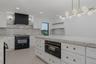 Kitchen featuring white shaker-style cabinetry, a contrasting matte black range hood, a dark finish freestanding range, and stone-surface countertops 