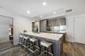 Kitchen featuring a white countertop island with an integrated sink, wood-finish cabinetry, recessed ceiling lighting, and wood-finish flooring