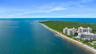 Aerial perspective of coastal multi-story residential buildings featuring immediate proximity to the shoreline and direct access to expansive sandy be