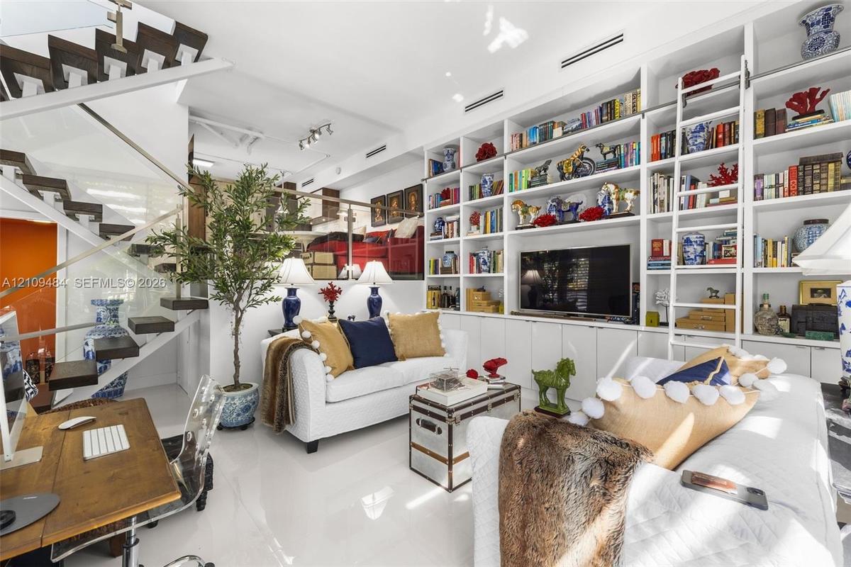 Custom floor-to-ceiling built-in cabinetry with integrated sliding library ladder, floating staircase with glass railings, and white gloss flooring
