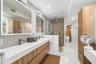 Floating dual-vanity with integrated sinks and wood-finish cabinetry, illuminated mirrored medicine cabinets, terrazzo-style wall surfacing, walk-in g