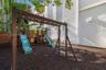 Outdoor space featuring a multi-component wooden play structure with dual slides, rubber mulch ground cover, and wood perimeter fencing