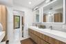 Floating double vanity with wood-finish cabinetry and integrated sinks, speckled stone-finish wall cladding, and dual recessed medicine cabinets with 