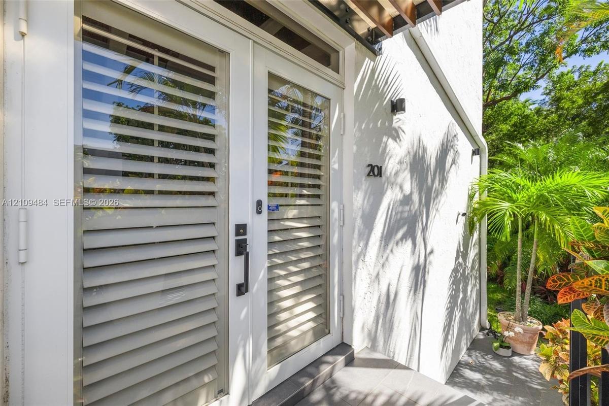 Exterior entrance featuring double glass-paneled doors with integrated horizontal louvers, a transom window, matte black hardware, and an overhead woo