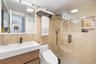 Bathroom featuring a wood-finish floating vanity with an integrated white sink, stone-tiled wall surfaces, a glass-enclosed shower with an integrated 