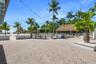 Outdoor space featuring a herringbone-patterned brick paver patio, thatched-roof tiki hut, built-in concrete planters, and perimeter string lighting