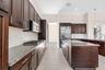 Kitchen featuring dark wood cabinetry, light granite countertops, a gas range, a mosaic tile backsplash, and stainless steel appliances