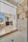 Glass-enclosed shower featuring large format wall tiles with a decorative mosaic accent and dual recessed niches