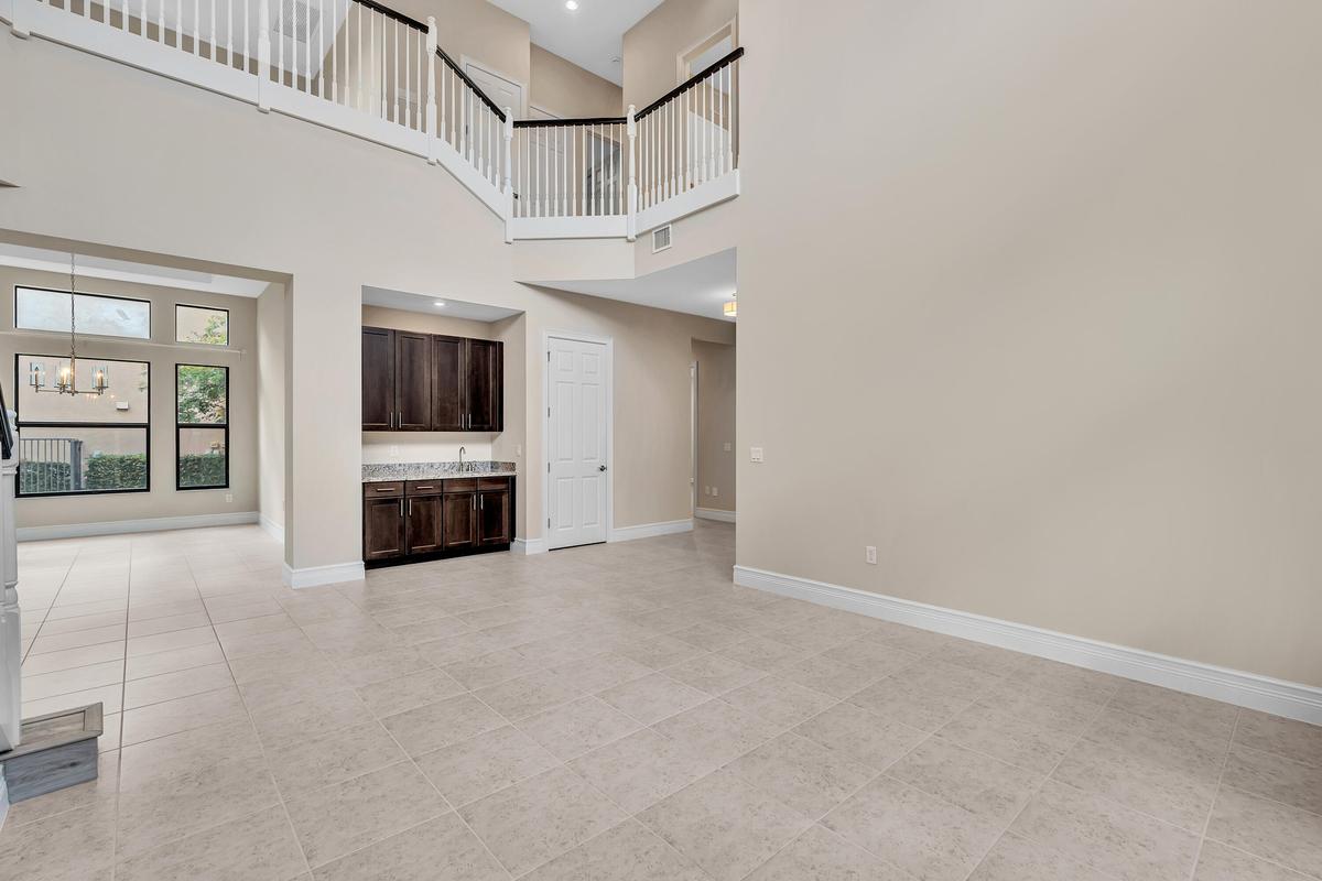 Spacious open-concept great room showcasing soaring two-story ceilings, abundant natural light from large multi-pane windows, neutral tile flooring th