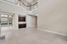 Spacious open-concept great room showcasing soaring two-story ceilings, abundant natural light from large multi-pane windows, neutral tile flooring th
