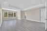 Spacious living area showcasing gleaming wood-finish flooring, a coffered ceiling with recessed lighting, and abundant natural light from triple-pane 