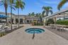 Resort-style outdoor entertaining space featuring a circular spa with integrated seating, expansive paved terrace, mature palm trees, pergola-covered 
