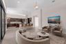Open-concept living space featuring a curved sectional sofa, wood-finish flooring throughout, and abundant natural light from expansive glass sliding 