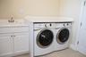 Dedicated laundry room featuring side-by-side front-load washers and dryers with stainless steel drums and digital controls, positioned beneath a soli