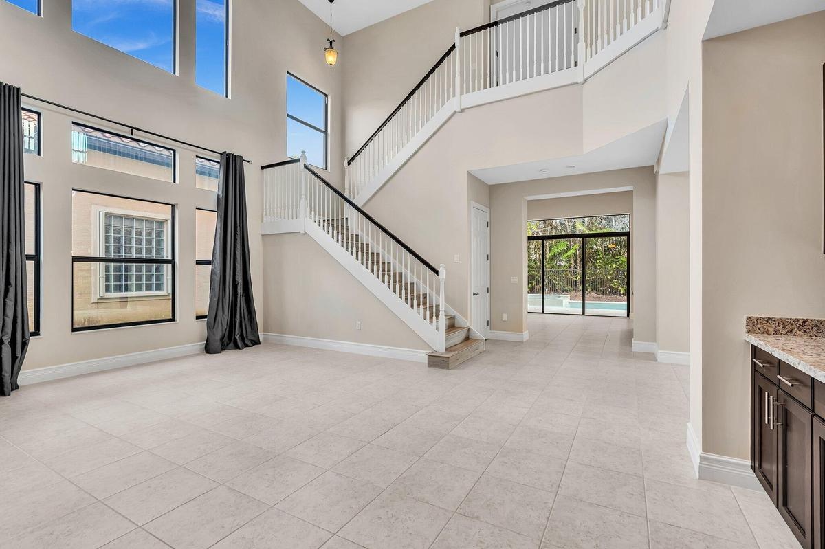 Soaring two-story foyer showcasing abundant natural light from expansive upper windows, elegant curved staircase with metal railings, light-finish til