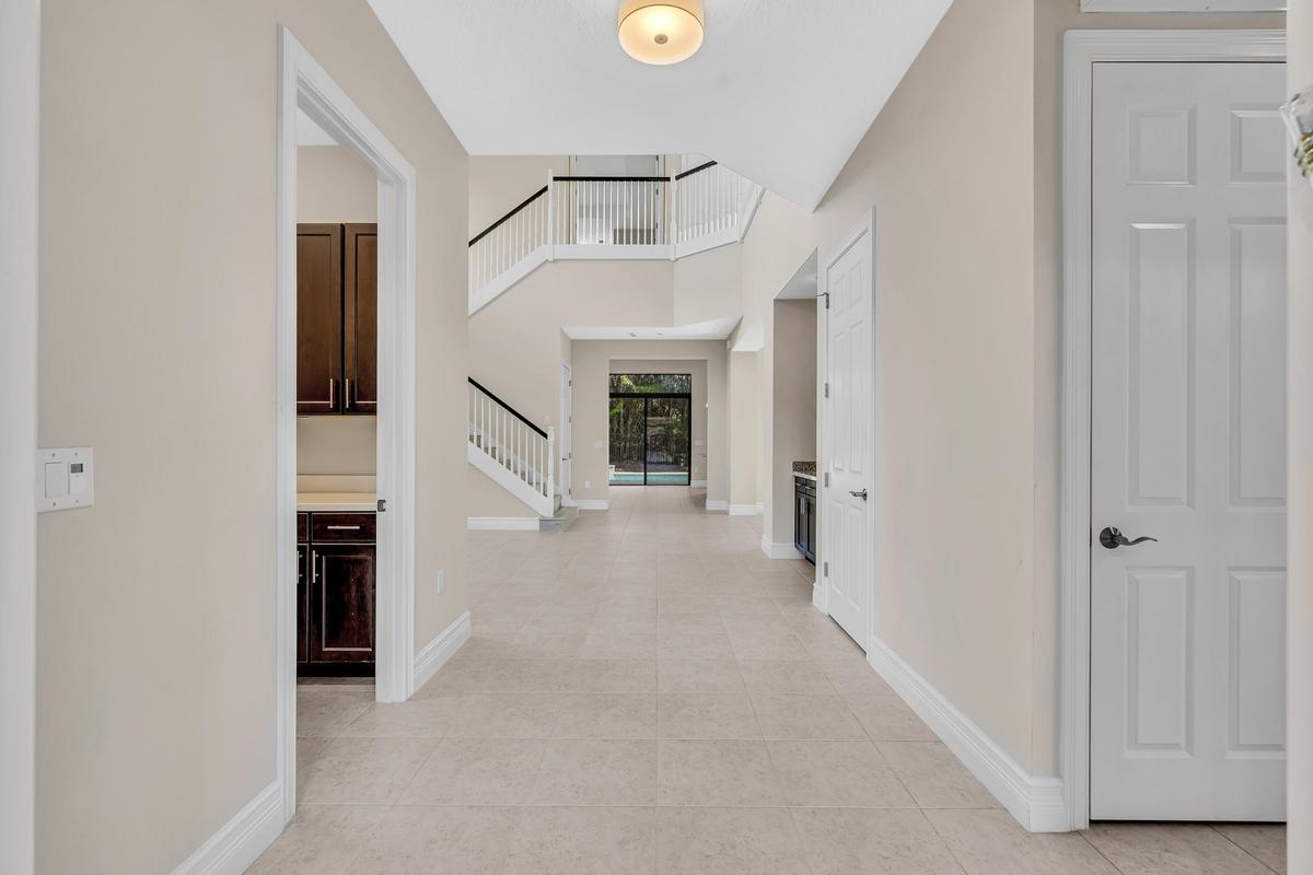 Bright two-story foyer featuring soaring ceilings, a curved staircase with white railings, neutral tile flooring throughout, and abundant natural ligh