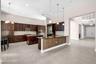 Spacious kitchen featuring dark wood cabinetry, a central island with a gas cooktop, double ovens, and a large breakfast bar with pendant lighting