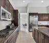 Galley-style kitchen featuring dark wood cabinetry, stainless steel appliances including a gas cooktop and side-by-side refrigerator, granite countert