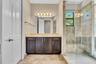 Spa-inspired primary bathroom featuring a dark wood vanity with multiple storage cabinets, marble-look countertops, and brass hardware