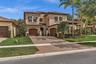 Tuscan-inspired stucco exterior featuring a barrel tile roof, arched windows with shutters, multiple garage bays with wood-finish doors, a paver drive