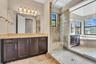 Spa-inspired primary bathroom featuring a double vanity with dark cabinetry and wood-finish countertop, paired with a large walk-in shower encased in 