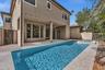 Resort-style backyard oasis featuring a sparkling saltwater pool with sun shelf, expansive composite decking, covered patio with multiple glass doors,