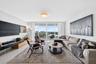 Living area featuring floor-to-ceiling glass doors, neutral tile flooring, flush-mount lighting, and exterior access to a balcony with water scenery